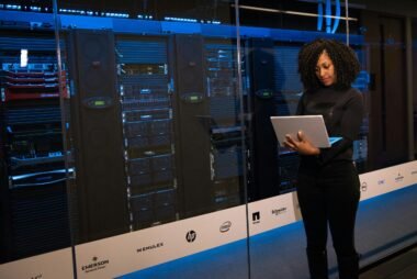 A female engineer using a laptop while monitoring data servers in a modern server room.